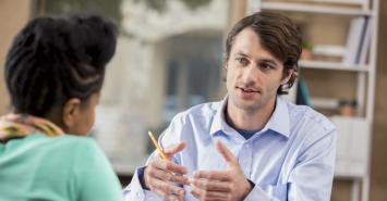 person explaining something to another person, holding a pencil and smiling