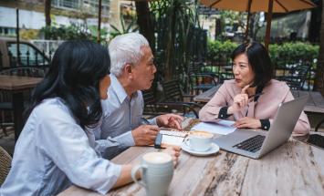 Three people at a table with a laptop and papers