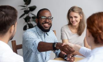 Person reaching across a desk and shaking someone's hand