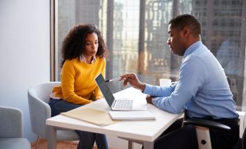 Two people on opposite sides of a table looking at a laptop