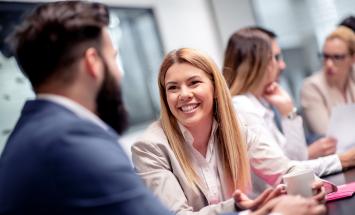 People sitting at a conference table and one of them is smiling at the camera